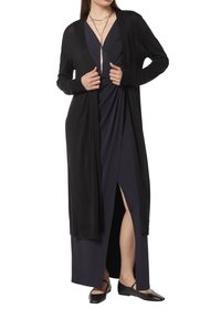 Długi czarny kardigan wykonany z lekkiego materiału, z luźnym krojem, otwartym przodem i pełnymi rękawami, nałożony na ciemną sukienkę.