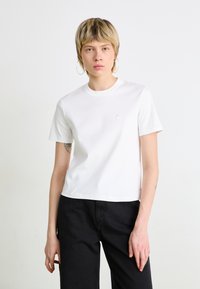 Hvid bomulds t-shirt med rund hals, korte ærmer og et lille logo på venstre bryst. Kombineret med sorte bukser. Enkelt, klassisk design.