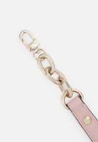 Maillons de chaîne en métal doré attachés à une lanière en cuir texturé rose avec un bouton doré et un crochet de fermeture sur un fond blanc.