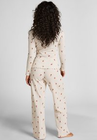 Crème-kleurige pyjama set gemaakt van zachte stof, met een aansluitend top met lange mouwen en bijpassende broek met wijde pijpen, beide voorzien van kleine bloemmotieven.
