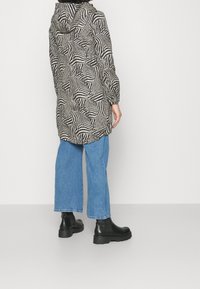 Giacca leggera a fantasia zebra realizzata in tessuto; presenta un cappuccio, maniche lunghe e una vestibilità comoda, abbinata a jeans larghi blu e stivali neri.