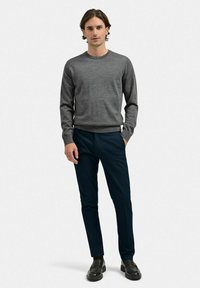 Grå stickad tröja med rund hals, bärs med mörkblå skräddarsydda byxor och svarta loafers. Slät yta, åtsittande design.