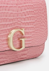 Borsa a tracolla in pelle rosa con finitura texturizzata a coccodrillo, dotata di hardware in metallo dorato a forma di lettera "G". Include una base liscia e bordi cuciti.