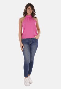 Top rosa in stile halter con scollatura arricciata, abbinato a jeans aderenti blu e sneakers bianche. Tessuto morbido e vestibilità rilassata.