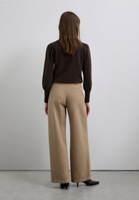 Suéter marrón de manga abullonada combinado con pantalones beige de tiro alto y pierna ancha. Calzado negro con tacón. Fondo neutro.