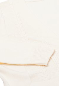 Krémový pletený cardigan s výstřihem do V, zdobený texturovanými vzory a žebrovanými manžetami. Měkká, lehká tkanina s útulným designem.