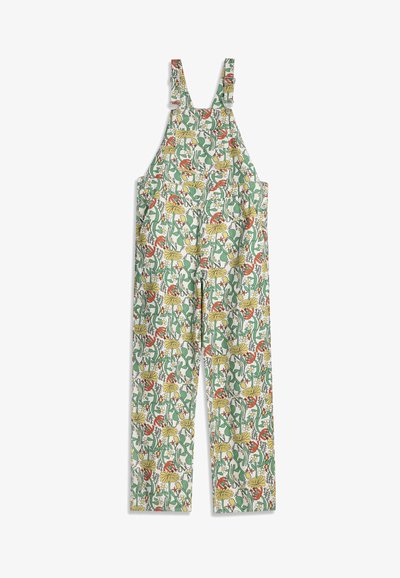 Salopette blanche à jambes larges, bretelles ajustables, avec un imprimé floral et feuillage coloré en tons verts, jaunes et rouges.