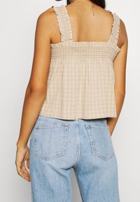 Top a quadretti beige con corpetto arricciato e spalline volantes, abbinato a jeans in denim blu chiaro con tasche posteriori e unfit rilassato.