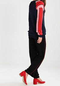 Marinfärgad sweatshirt med röd och rosa randiga ärmar, kombinerad med svarta byxor med röda sidostripes och röda högklackade skor.