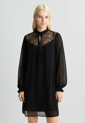 Abito nero con scollo in pizzo trasparente e lunghe maniche a sbuffo. Presenta un colletto arricciato e delicate decorazioni a bottoni lungo la parte anteriore. Tessuto morbido e fluido.