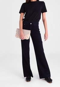 Černé tričko, tmavě modré široké džíny s vysokým pasem, držící béžovou psaníčko kabelku a černé boty s mírným podpatkem. Jednoduchý a ležérní design.