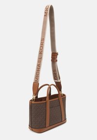 Hnedá taška cez rameno s monogramom MK, hnedé kožené akcenty, dvojité uško a odnímateľný ramenný popruh s nápisom "MICHAEL KORS" v béžovej farbe.