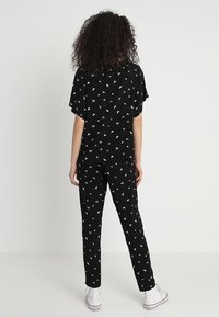 Svart loungewear-set som består av en t-shirt med kort ärm och byxor med ett vitt fågelmönster, tillverkat av ett mjukt tyg med en avslappnad passform.