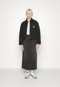 Schwarze cropped Jacke mit einem goldenen Reißverschluss, weißes Oberteil und hoch taillierter schwarzer Jeansrock. Weiße und gelbe Sneakers runden das Outfit ab.