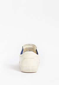 Baskets blanches avec accents bleus, matériau en daim, finition texturée, semelle plate et col rembourré. Marque visible sur le talon.