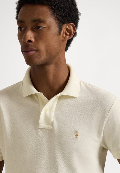 Πόλο μπλουζάκι σε ανοιχτόμπεζ βαμβάκι με υφασμάτινη υφή. Διαθέτει γιακά, τριπλό κούμπωμα με κουμπιά και κεντημένο λογότυπο στο στήθος.