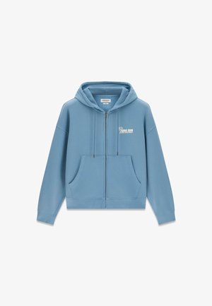 Lichtblauwe zip-up hoodie met zakken aan de voorkant en "Malibu Guess Jeans Company" logo op de linkerborst, voorzien van een capuchon met trekkoord.