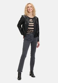 Czarny faux skórzany kurtka z okrągłym dekoltem, zestawiona z paskowanym topem i szarymi dżinsami. Modelka nosi czarne botki za kostkę.