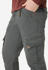 Cargo pants in textured dark gray fabric, featuring side pockets with flaps, a zippered pocket, and accent stitching.