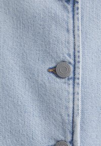 Hellblaues Jeanshemd mit Knopfleiste, silbernem Zubehör, sichtbaren Nähten und einem strukturierten Stoff mit einem dezenten gestreiften Muster.