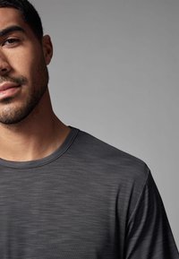 Camiseta deportiva gris oscuro con cuello redondo, confeccionada en un tejido suave y texturizado con un ligero brillo, que presenta un corte relajado en los hombros.