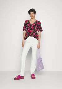 Top preto florido com decote em V, calças brancas e sapatos rosa-choque. A modelo também carrega uma bolsa de malha roxa clara.
