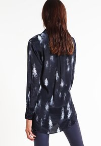 Chemise noire à manches longues avec un motif de forêt en blanc et gris. Tissu lisse, poignets à boutons et ourlet incurvé. Vue de dos.