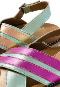 Sandales à bout ouvert avec des brides en cuir métallisé rose, vert menthe et or et des fermetures réglables à la cheville sur semelles couleur beige.