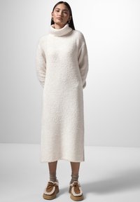 Vestito a maglia bianco lungo, comodo, con maniche lunghe e colletto alto, tessuto testurizzato, vestibilità dritta e spacchi laterali, abbinato a scarpe marroni senza lacci.