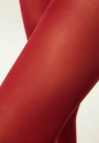 Röda strumpbyxor med en slät, ogenomskinlig textur, som har ett fint, jämnt stickat mönster som framhäver benens form. Inga synliga sömmar eller metalldetaljer.