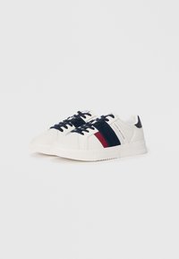 White canvas sneakers featuring navy and red stripes, lace-up design, textured rubber sole, and branding on the tongue.