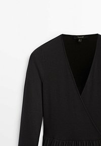 Robe noire portefeuille à manches longues, texture côtelée, décolleté en V profond et bas évasé, avec un buste lisse et ajusté et un ourlet fluide.