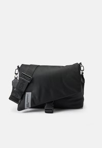 Borsa a tracolla nera realizzata in nylon liscio, con una patta pieghevole, tracolla regolabile con logo e un piccolo tag con marchio.