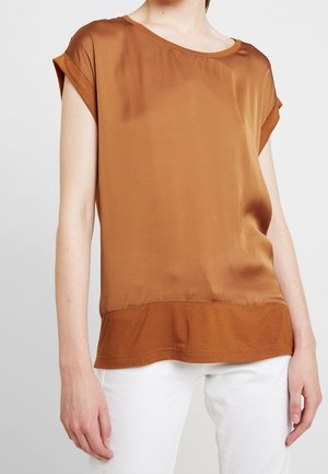 Top corto de satén marrón con cuello redondo y textura de dobladillo en contraste, combinado con pantalones blancos. Acabado suave y corte relajado.
