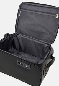 Schwarzer Hartschalenkoffer mit strukturiertem Äußeren, Reißverschluss und einem Innenraum, der eine Netztasche und Gurte zur Sicherung von Gegenständen bietet.
