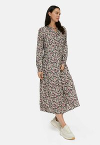 Floral jurk met lange mouwen op een donkere achtergrond, met roze en witte bloemen, een v-halslijn en een gelaagde zoom. Gepaarde met lichte sneakers.