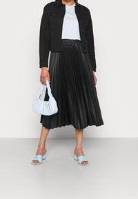 Giacca di jeans nera, top bianco corto, gonna midi nera plissettata, borsa a tracolla blu chiaro e sandali con tacco blu. Focalizza su texture e forme.