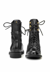 Para czarnych skórzanych botków za kostkę z wiązaniem, z złotymi oczkami, przedstawionych z przodu i z tyłu na białym tle.