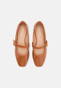 Paire de chaussures style Mary Jane marron brillant avec bouts carrés et brides à boucle, vues de dessus sur un fond uni.