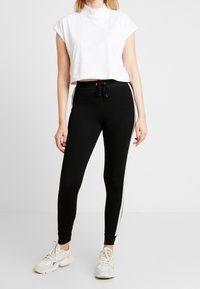Svarta leggings med vita sidostråk, kombinerade med en kortärmad vit t-shirt. Leggingsen har dragsko i midjan och en figurnära design.