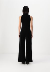 Black velvet jumpsuit with a high neckline, fitted bodice, and wide-leg pants. Smooth texture and minimalist design, suitable for various occasions.