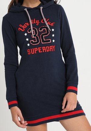 Navy blue long-sleeve hoodie dress with red and white "Varsity Club 32 Superdry" text and star designs, red striped cuffs and hem.