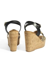 Sandales compensées en cuir noir avec talons en liège, présentant un motif tissé et une sangle ajustable à la cheville. La surface texturée du talon ajoute une touche de détail.