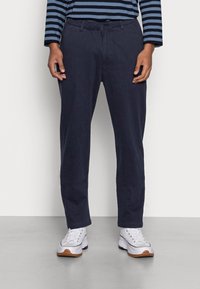 Marina blå byxor med rak skärning, gjorda av mjukt tyg, med knappstängning och bältesöglor, ihop med vita sneakers.