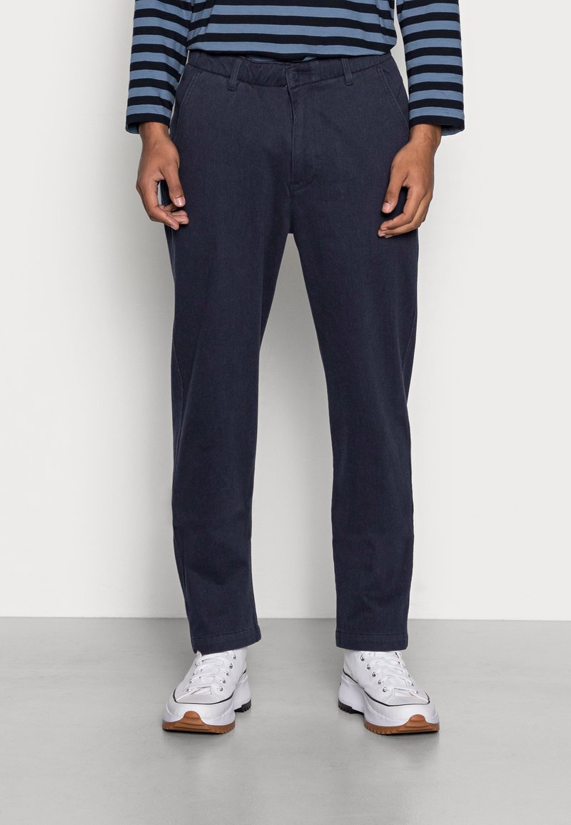 Marina blå byxor med rak skärning, gjorda av mjukt tyg, med knappstängning och bältesöglor, ihop med vita sneakers.