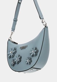 Borsa sintetica azzurro chiaro con design curvo, decorazioni a strati a forma di fiore, borchie argentate e un logo metallico sulla parte anteriore. Incluso un manico regolabile.