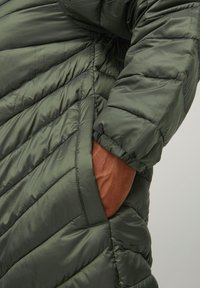 Chaqueta de plumas verde con un diseño acolchado, que presenta costuras horizontales y un bolsillo lateral. El material tiene una textura suave y brillante.