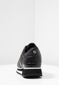 Černé kožené tenisky s texturovaným bočním panelem, kovovým logem a kontrastní bílou mezipodešví. Mají zaoblenou patu a polstrovaný límec.