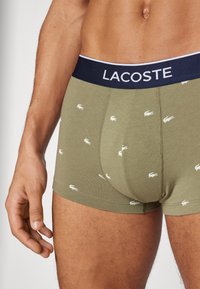 Olivazöld boxernadrág s�ötétkék derékkal, amelyen a "LACOSTE" logó található, kisméretű fehér aligátor mintákkal díszítve és puha tapintású.