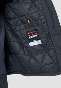 Interno della giacca nera trapuntata con etichette Primaloft e K-Way. Presenta motivi a diamante e una piccola tasca con chiusura a bottone.